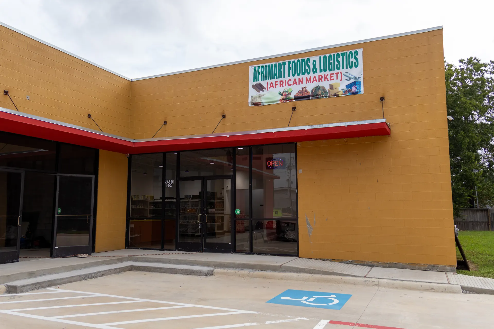 Storefront of Afrimart grocery store in Houston, with a red awning, glass entrance, and lit OPEN sign