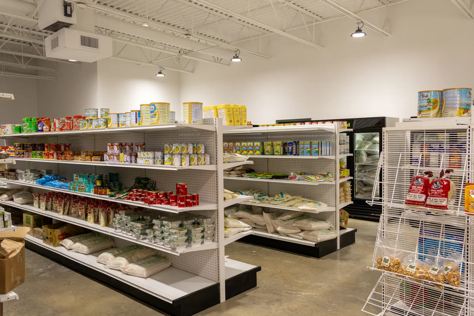 Grocery aisle at Afrimart with shelves of rice, beans, and canned milk, and a frozen food case in the back